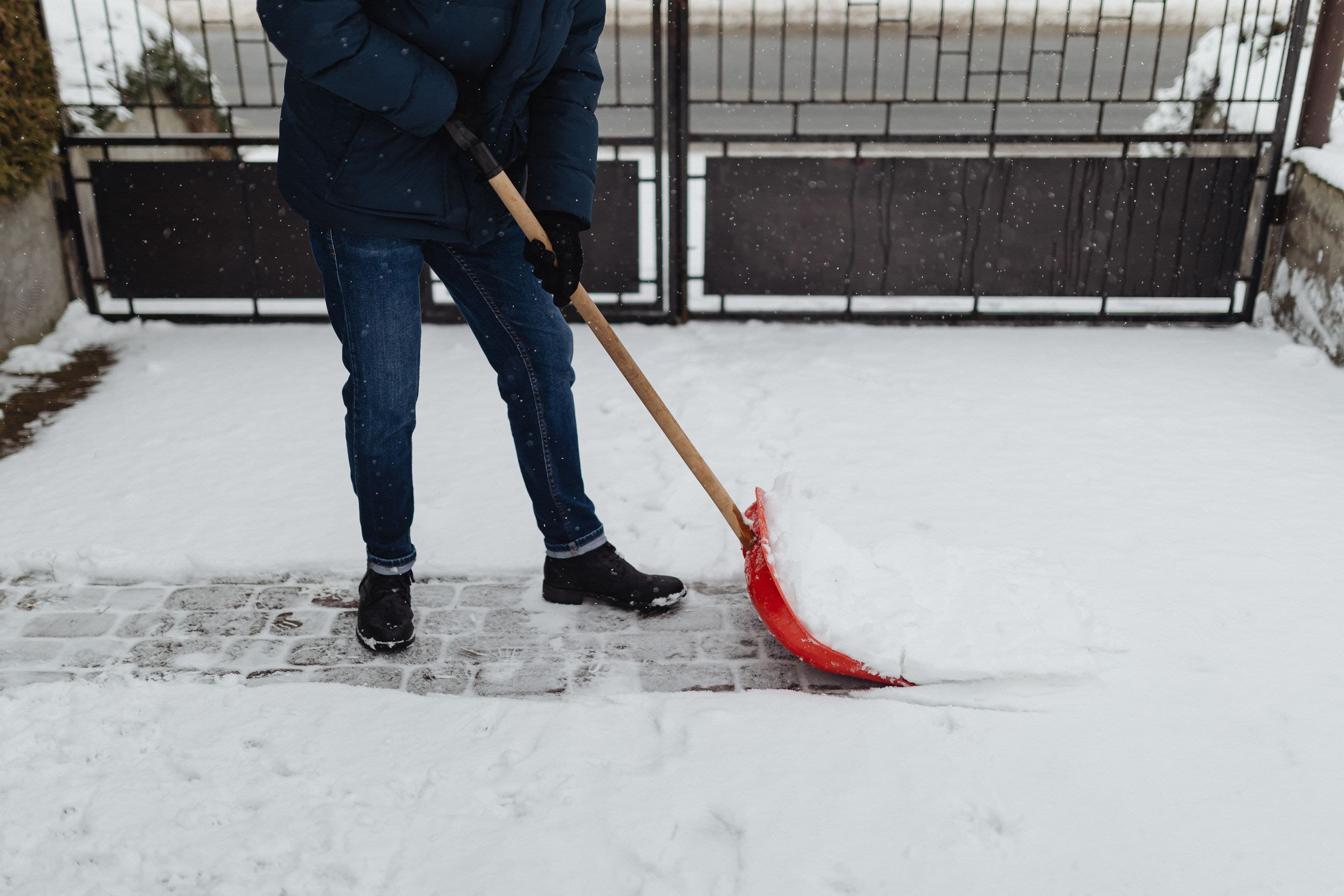 Schneeräumen auf einer gepflasterten Einfahrt vor dem Tor